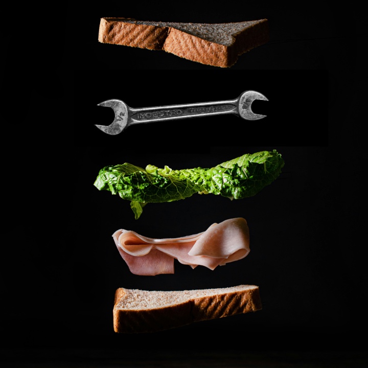 Components of a sandwich in an exploded vertical stack, including lettuce and a spanner.